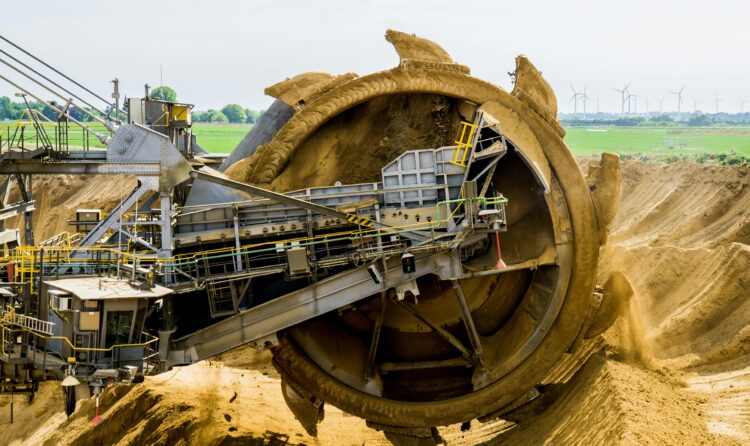 A large bucket wheel excavator working in an open pit mine against a green landscape.
